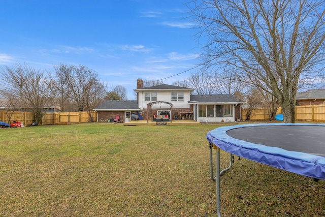 back of house featuring a sunroom, a trampoline, and a lawn