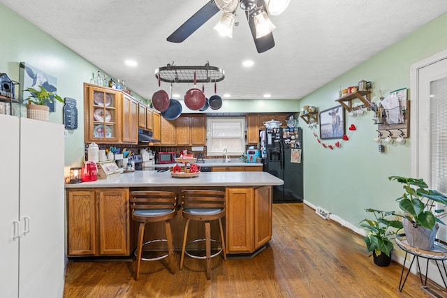 kitchen featuring sink, dark wood-type flooring, a kitchen bar, black fridge with ice dispenser, and kitchen peninsula