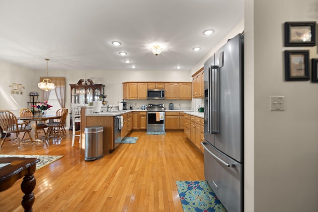 kitchen with pendant lighting, sink, appliances with stainless steel finishes, an inviting chandelier, and light hardwood / wood-style floors