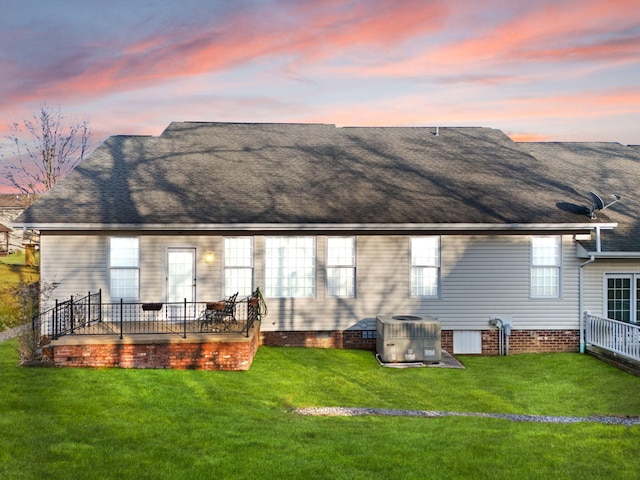 back house at dusk featuring cooling unit and a lawn