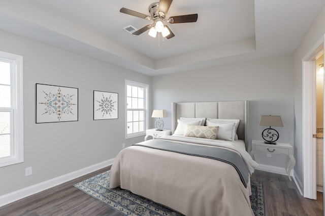 bedroom with a raised ceiling, dark wood-type flooring, and ceiling fan