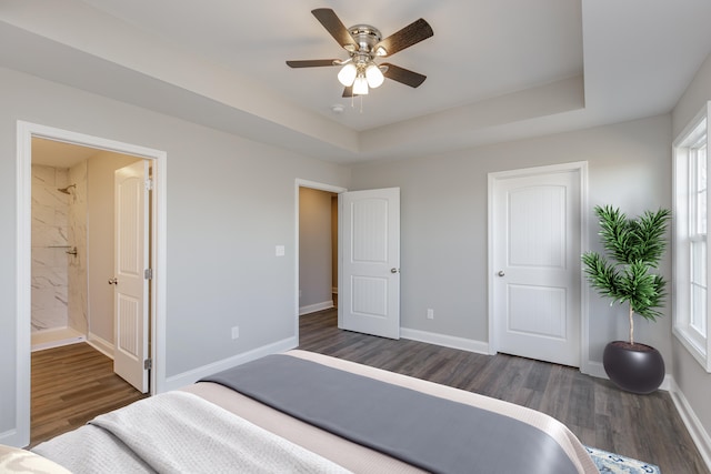 bedroom featuring dark hardwood / wood-style floors, ensuite bathroom, and a tray ceiling