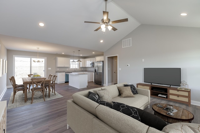 living room with dark hardwood / wood-style flooring, ceiling fan with notable chandelier, and high vaulted ceiling