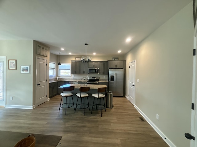 kitchen with a breakfast bar area, decorative light fixtures, a center island with sink, appliances with stainless steel finishes, and dark hardwood / wood-style floors