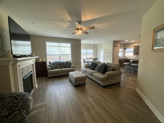 living room with dark wood-type flooring, ceiling fan with notable chandelier, and a fireplace