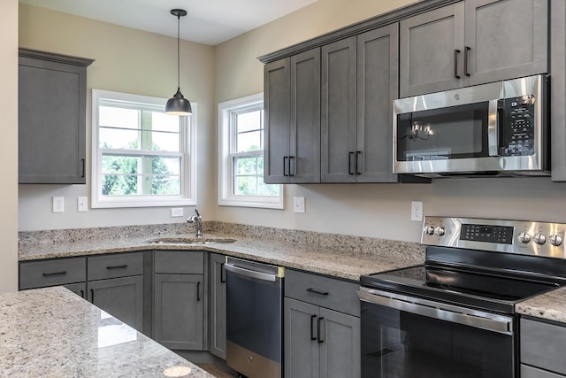 kitchen with gray cabinets, decorative light fixtures, sink, stainless steel appliances, and light stone countertops