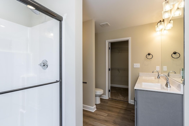 bathroom with a shower with door, an inviting chandelier, hardwood / wood-style floors, vanity, and toilet