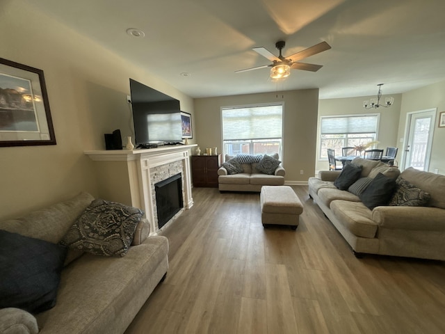 living room featuring ceiling fan with notable chandelier, a stone fireplace, and hardwood / wood-style floors