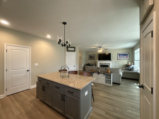 kitchen featuring pendant lighting, hardwood / wood-style flooring, gray cabinetry, a center island, and light stone countertops