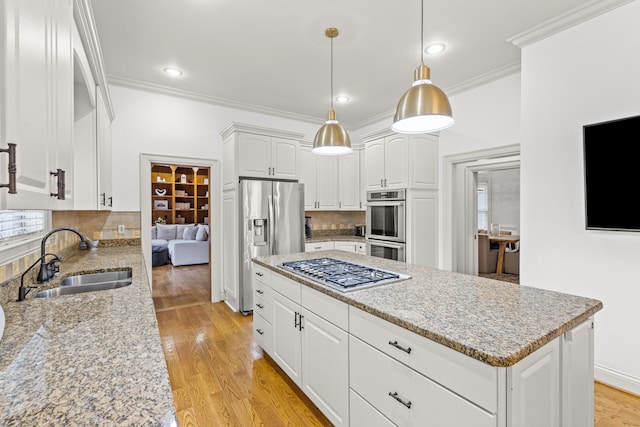 kitchen with sink, white cabinetry, stainless steel appliances, light stone counters, and decorative light fixtures