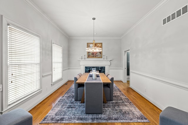 dining room featuring a fireplace, a notable chandelier, wood-type flooring, and ornamental molding