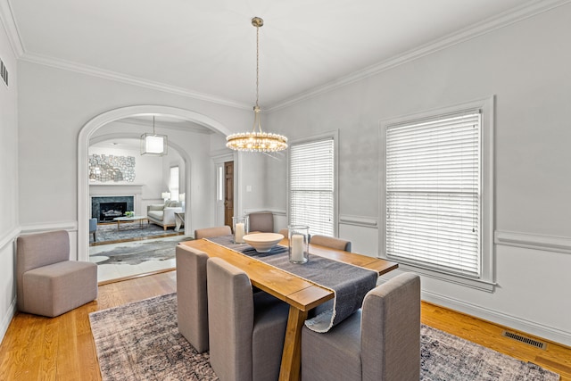 dining area with a premium fireplace, ornamental molding, an inviting chandelier, and light hardwood / wood-style flooring