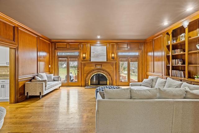 living room featuring wood walls, ornamental molding, a fireplace, and light wood-type flooring