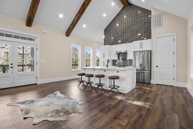 kitchen featuring white cabinetry, stainless steel fridge, a kitchen breakfast bar, a kitchen island with sink, and dark wood-type flooring