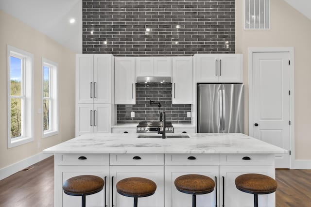 kitchen with white cabinetry, light stone countertops, a breakfast bar, and stainless steel fridge