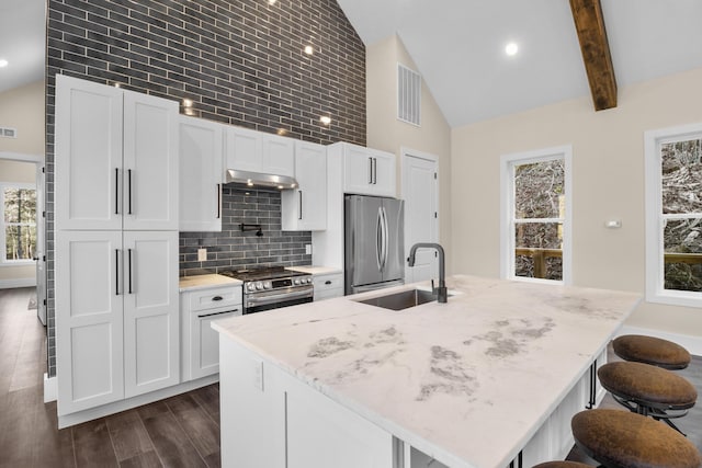 kitchen featuring an island with sink, sink, white cabinets, light stone counters, and stainless steel appliances