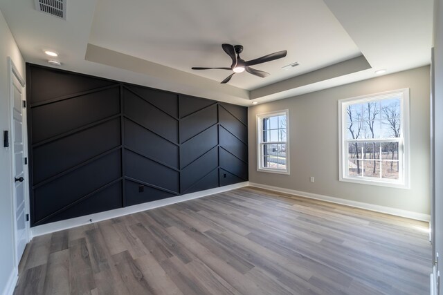 unfurnished bedroom featuring ceiling fan, a tray ceiling, a spacious closet, and light wood-type flooring