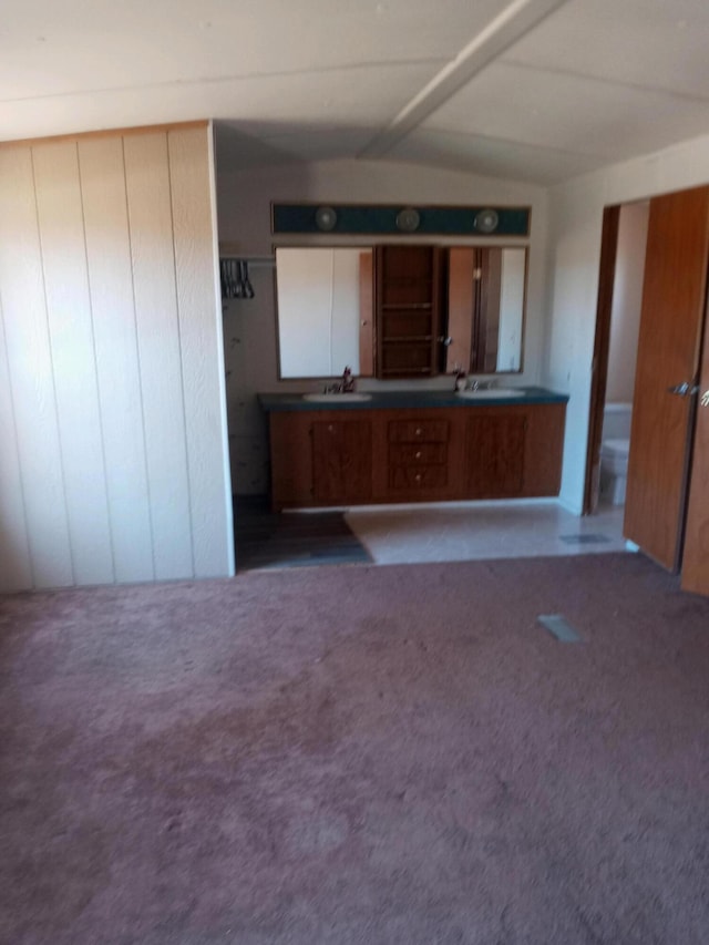 kitchen with a sink, lofted ceiling, dark countertops, and carpet flooring