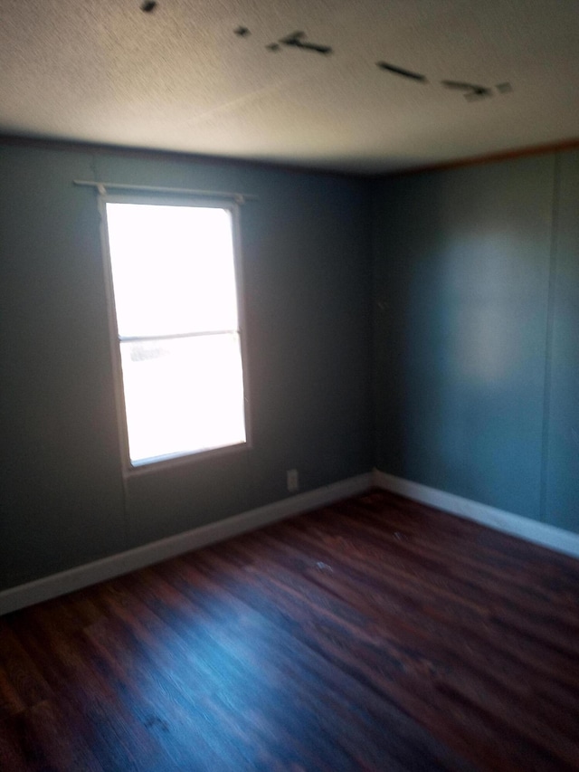 empty room with baseboards, a textured ceiling, and wood finished floors