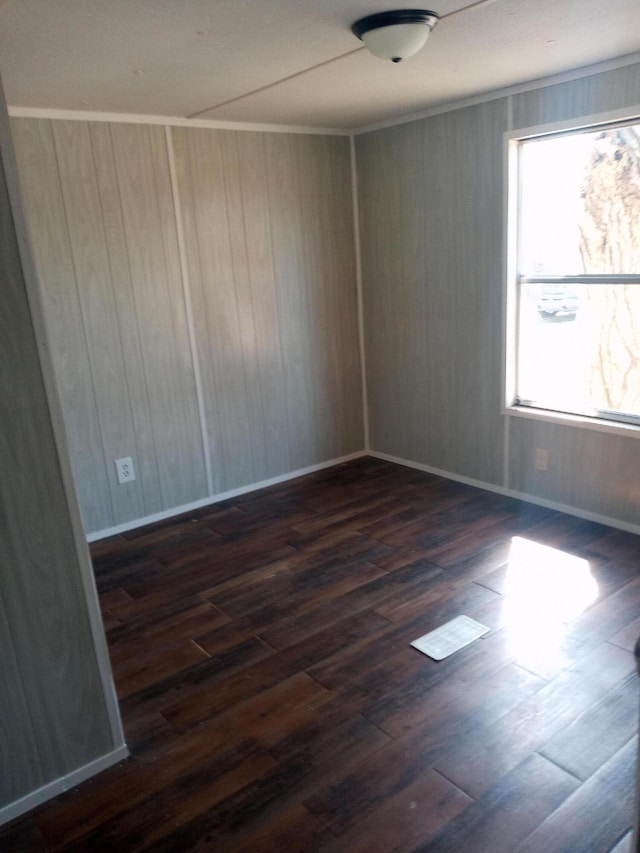 empty room featuring dark wood-style floors, baseboards, and ornamental molding