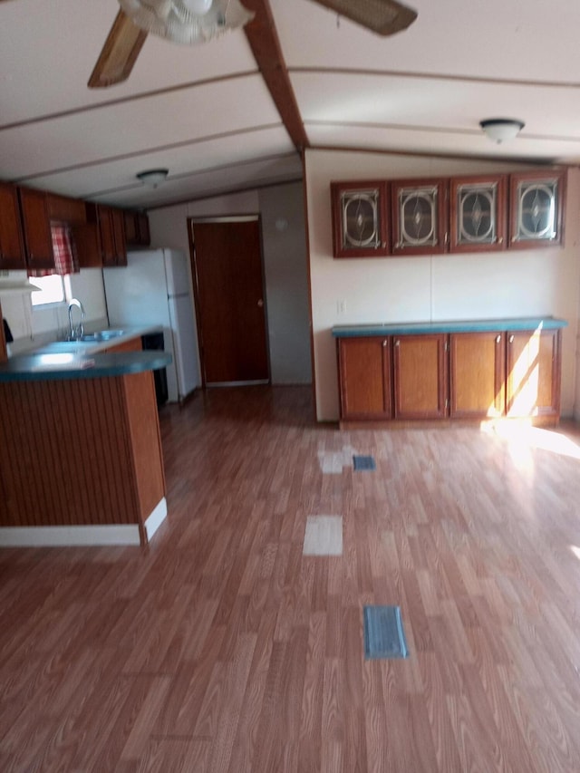 kitchen featuring brown cabinetry, a ceiling fan, light wood-style flooring, freestanding refrigerator, and a sink