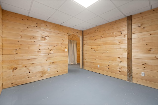 empty room with concrete flooring, a paneled ceiling, and wooden walls