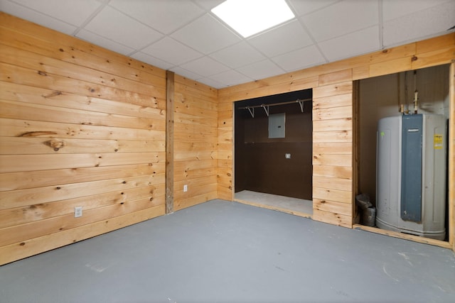 basement with a paneled ceiling, wooden walls, electric panel, and water heater