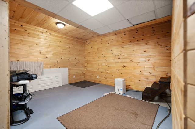 misc room featuring wooden walls, concrete flooring, and a paneled ceiling