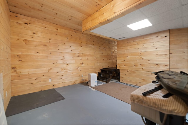 miscellaneous room with concrete flooring, a drop ceiling, and wood walls