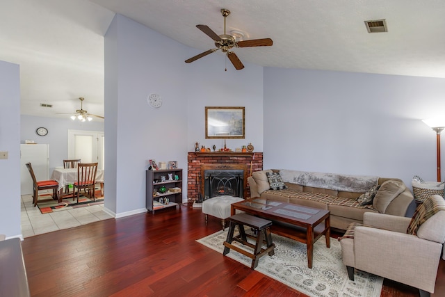 living room featuring visible vents, ceiling fan, lofted ceiling, a fireplace, and wood finished floors