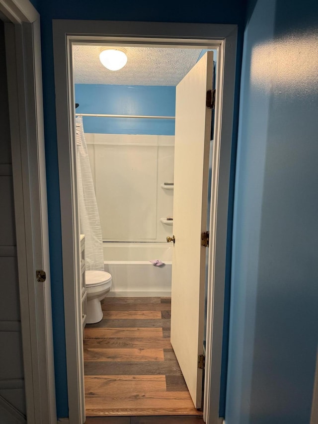 bathroom with hardwood / wood-style flooring, shower / bath combination with curtain, a textured ceiling, and toilet