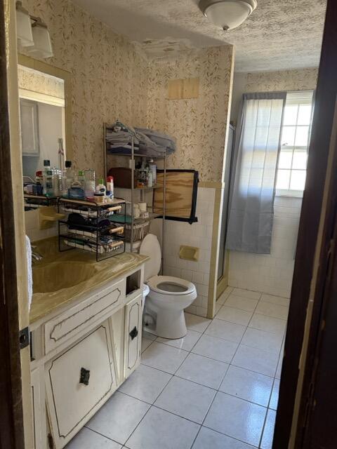 bathroom featuring tile walls, vanity, a textured ceiling, tile patterned floors, and toilet