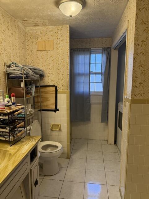 bathroom featuring toilet, tile patterned flooring, a textured ceiling, and tile walls