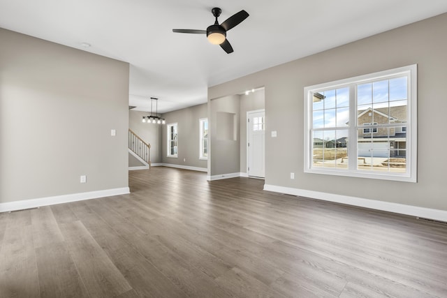 unfurnished living room featuring a ceiling fan, stairway, baseboards, and wood finished floors