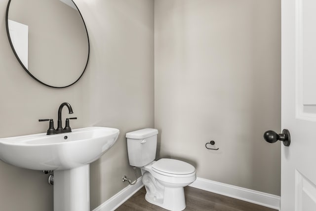 half bathroom with wood finished floors, toilet, and baseboards