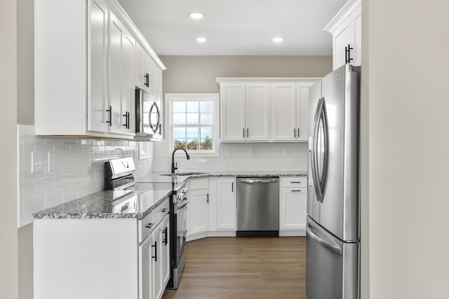 kitchen with stone countertops, appliances with stainless steel finishes, wood finished floors, white cabinetry, and a sink