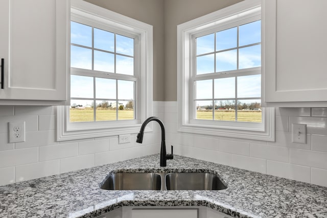 kitchen with light stone countertops, tasteful backsplash, white cabinetry, and a sink