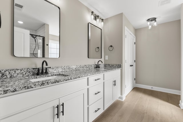 full bath with double vanity, visible vents, a sink, and wood finished floors