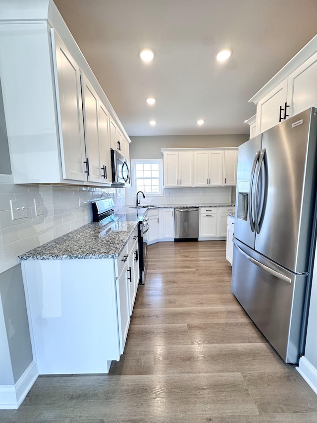 kitchen with white cabinetry, sink, dark stone countertops, stainless steel appliances, and light wood-type flooring