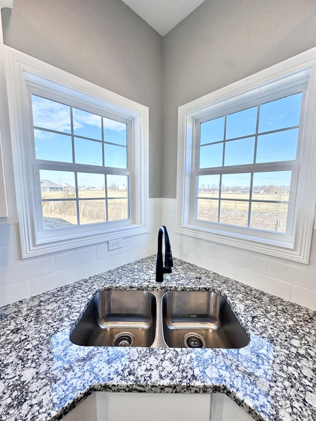 room details featuring sink, decorative backsplash, and stone countertops