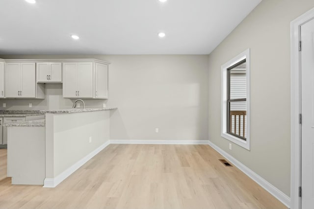 kitchen featuring light stone countertops, white cabinets, light hardwood / wood-style floors, and kitchen peninsula