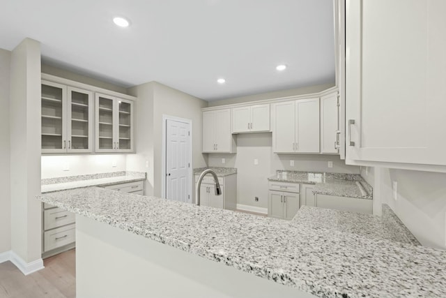 kitchen with white cabinetry, light stone countertops, sink, and light wood-type flooring