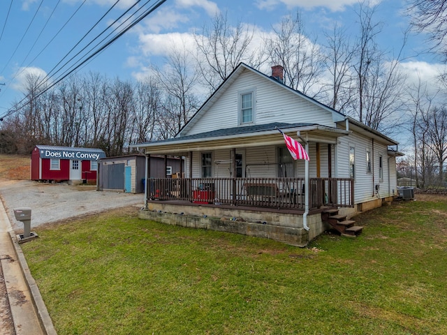 view of front of house with cooling unit, a storage shed, a front lawn, and covered porch