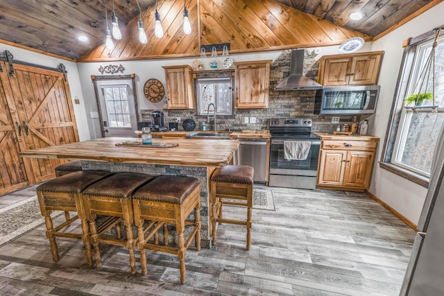 kitchen with butcher block countertops, wooden ceiling, appliances with stainless steel finishes, a barn door, and wall chimney range hood