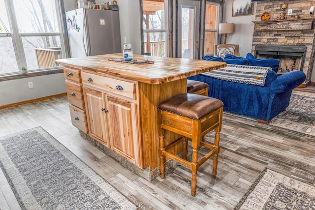 kitchen with a kitchen island, a stone fireplace, stainless steel refrigerator, butcher block counters, and light hardwood / wood-style flooring