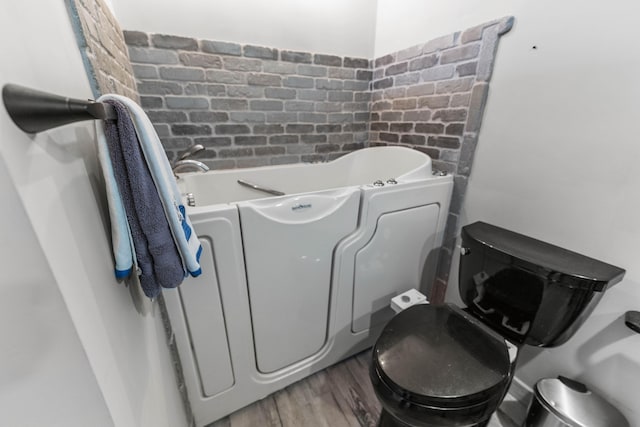 bathroom featuring a tub to relax in, brick wall, hardwood / wood-style floors, and toilet