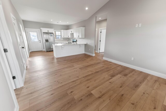 kitchen with light wood-type flooring, stainless steel fridge, a kitchen breakfast bar, kitchen peninsula, and white cabinets