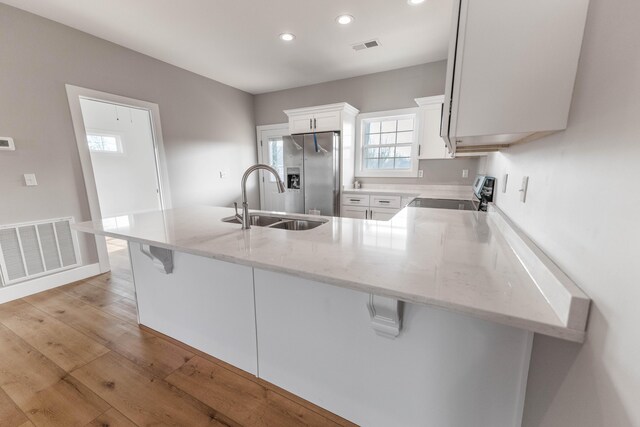 kitchen featuring white cabinetry, sink, light hardwood / wood-style floors, kitchen peninsula, and stainless steel appliances