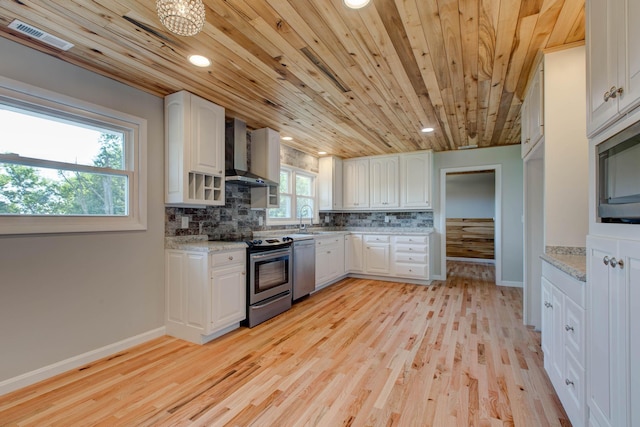 kitchen with sink, white cabinetry, appliances with stainless steel finishes, light stone countertops, and wall chimney range hood