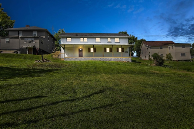 back house at dusk featuring a porch and a lawn